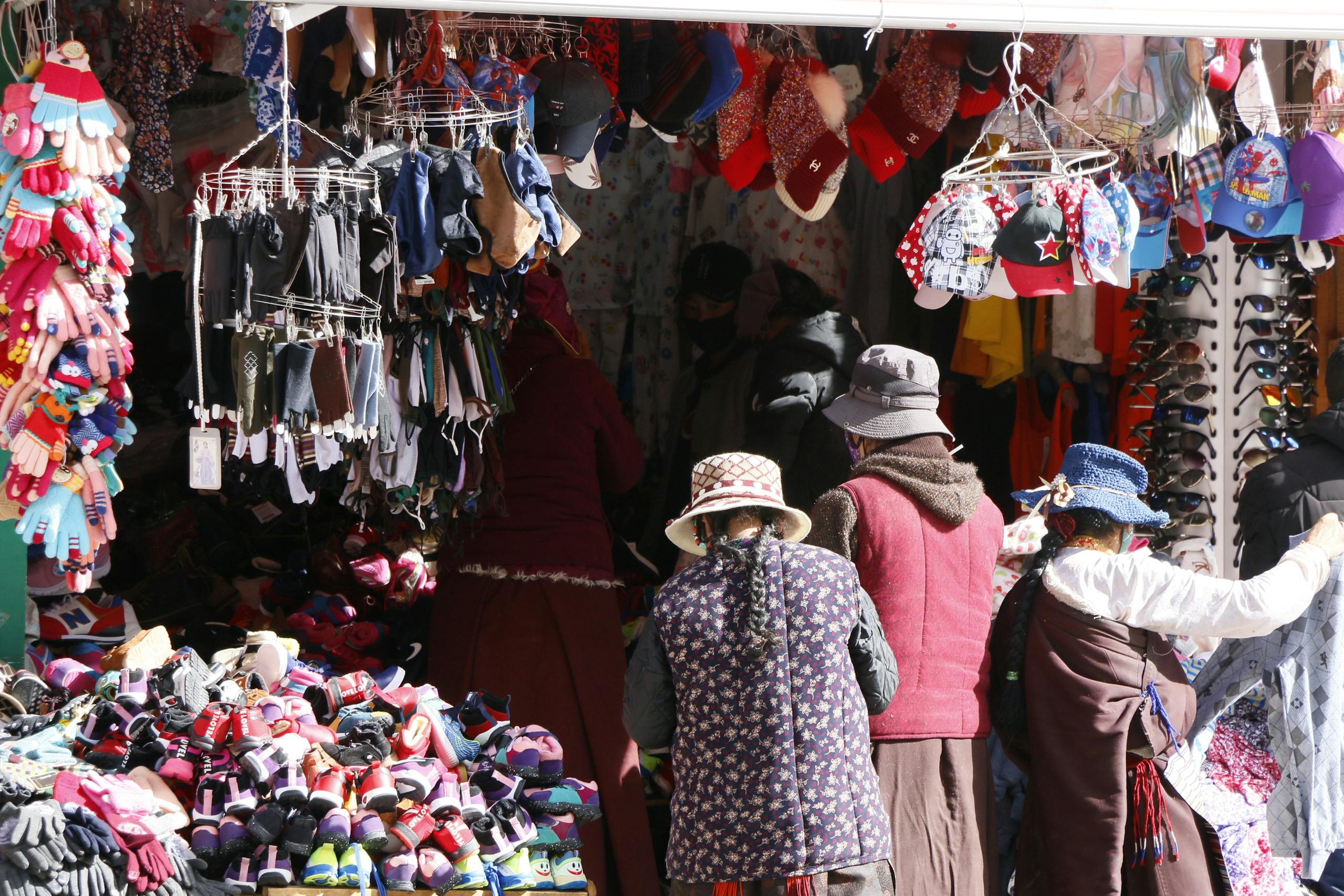 People shopping at an outdoor market stall filled with colorful winter clothing and accessories.